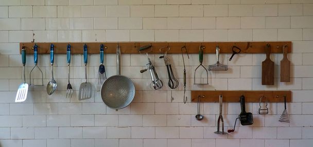Velhos utensílios de cozinha pendurados na parede da cozinha de azulejos brancos - Foto, Imagem