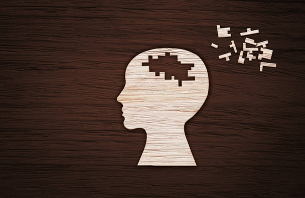 Mental health symbol. Human head silhouette with a puzzle cut out from wooden background - Фото, зображення