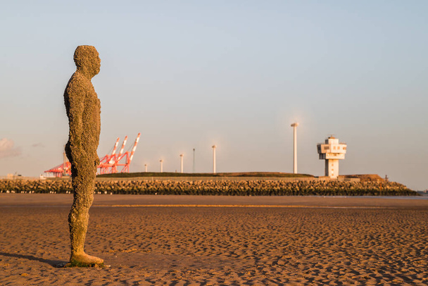 Een standbeeld van Iron Man op het strand bij Crosby bij Liverpool (Engeland) in juli 2020 voor een rij draaiende windturbines in Liverpool dock. - Foto, afbeelding