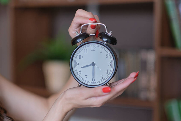женские руки с красным маникюром держат черный будильник. концепция управления временем - Фото, изображение