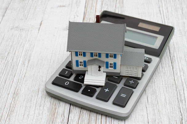 Casa modelo con una calculadora en escritorio de madera para mensaje hipotecario y relacionado con costos - Foto, imagen