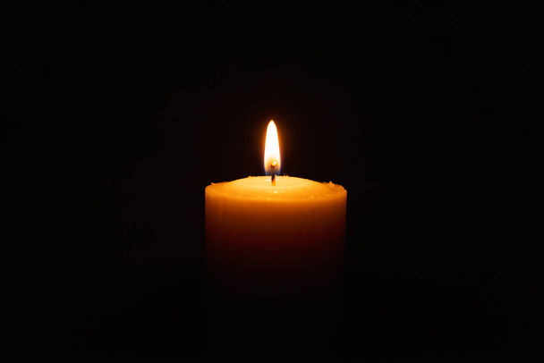Eine einzige Kerze brennt hell im schwarzen Hintergrund. Geistliche Kerze gelbe Flamme. Kerzenflamme in der Dunkelheit. - Foto, Bild