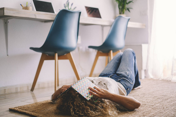 Giovane donna che dorme sul tappeto a casa con computer della postazione di lavoro in background. - Foto, immagini