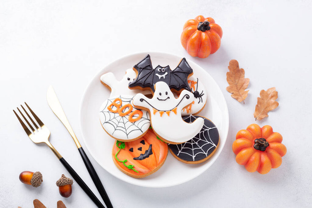Halloween table setting with gingerbread cookies on white plate and cuterly on white background. Bright homemade cookies for Halloween party - Фото, изображение