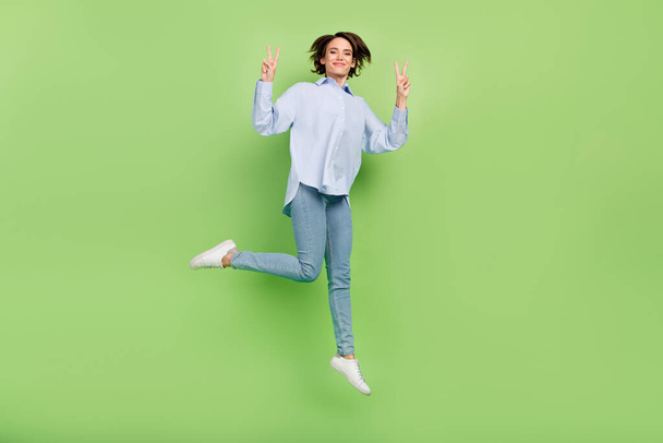 Full body photo of cheerful young positive happy woman jump up make v-sign isolated on green color background - Foto, imagen