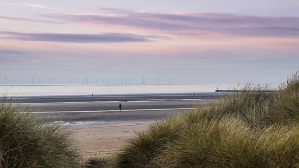 Una imagen de gran angular capturada a través de las dunas de arena en la playa de Crosby de cuatro de las figuras que conforman Another Place, una instalación de cien figuras de hierro creadas por Antony Gormley. - Foto, imagen