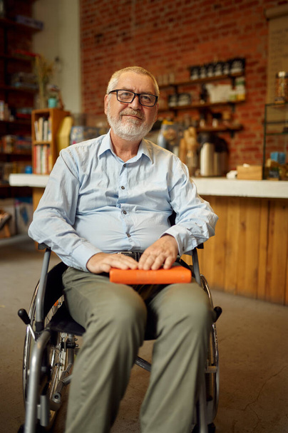 Uomo adulto disabile in sedia a rotelle tiene un libro - Foto, immagini