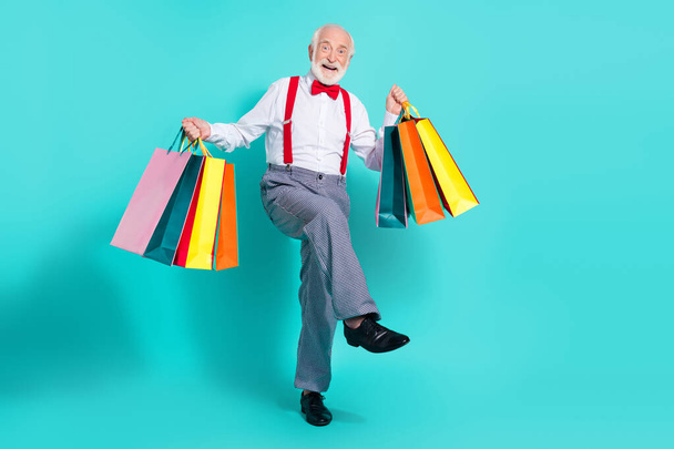 Full length body size view of nice cheerful grey-haired man holding new things dancing isolated over bright teal turquoise color background - 写真・画像