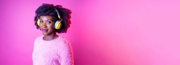 Portrait young black woman looking over listening music wireless headphones smiling happy and serene advertising copyspace background - Foto, afbeelding