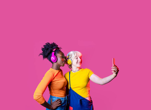 Дві молоді різноманітні жінки найкращі друзі ізольовані рекламні копії простору, що приймають селфі за допомогою смартфона
 - Фото, зображення