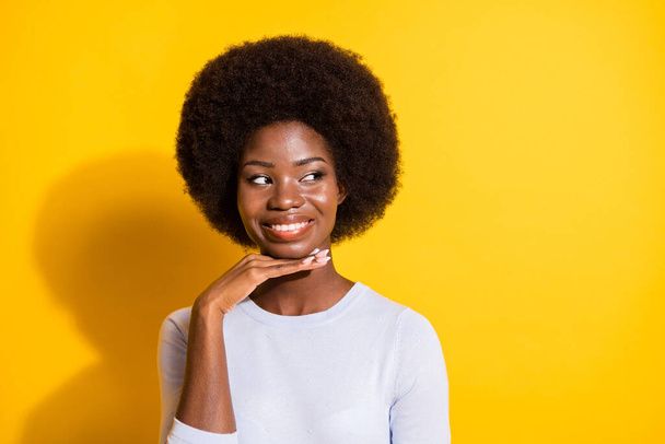 Portrait of adorable cheerful dark skin lady hand under chin look empty space isolated on yellow color background - Zdjęcie, obraz