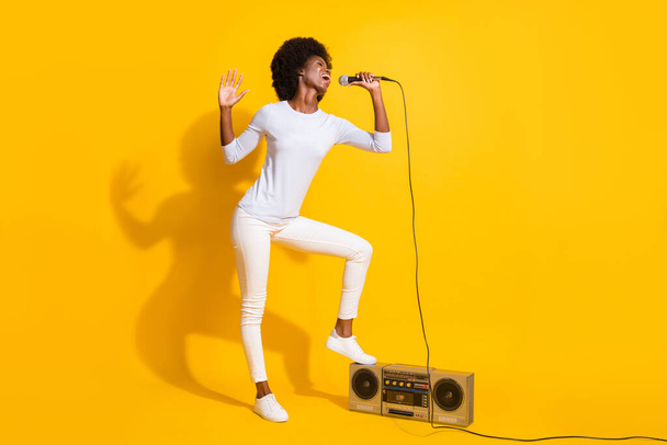 Full size photo of carefree excited dark skin lady singing leg on boombox isolated on yellow color background - Φωτογραφία, εικόνα