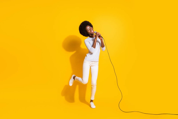 Full size photo of optimistic short hair lady sing in mic wear white pullover trousers sneakers isolated on yellow background - Foto, Imagen