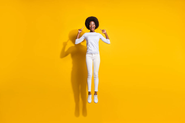 Full length photo of happy brunette afro american girl jump up point hair isolated on yellow color background - Foto, Imagen
