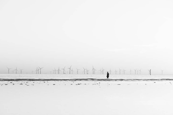 Железный человек был замечен на пляже в Кросби во время прилива в апреле 2021 года, стоящим лицом к ветровой ферме Бурбобанка. Он является частью "Другого места", художественной инсталляции возле Ливерпуля, состоящей из 100 статуй Железных людей, созданных Антонием Гормли.. - Фото, изображение
