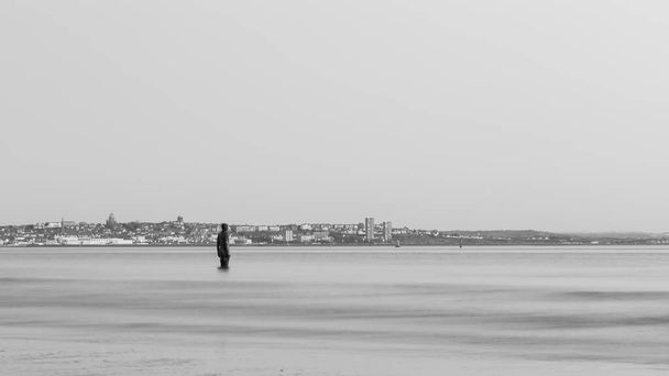 Залізна людина в чорно-білому, яку видно перед півостровом Віррал. Це частина іншого місця, арт-інсталяція на пляжі Кросбі біля Ліверпуля, що складається зі 100 статуй Залізних Людей, створених Антонієм Гормлі. Його було захоплено на заході сонця у квітні. - Фото, зображення