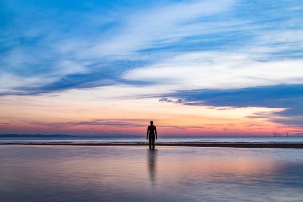 An Iron Man captured at sunset in April 2021 as the tide comes in.  He is part of Another Place, the art installation near Liverpool made up of 100 Iron Men statues created by Antony Gormley. - Foto, imagen