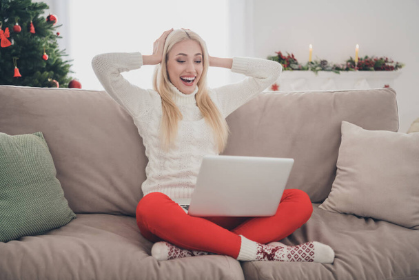 Photo of sweet impressed young woman dressed white sweater looking modern device hands arms head indoors room home house - Photo, Image
