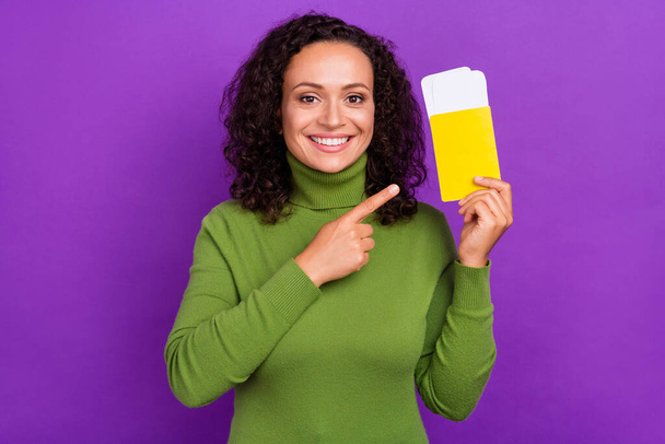 Photo of adorable attractive afro woman wear green turtleneck pointing finger plane tickets smiling isolated purple color background - Valokuva, kuva