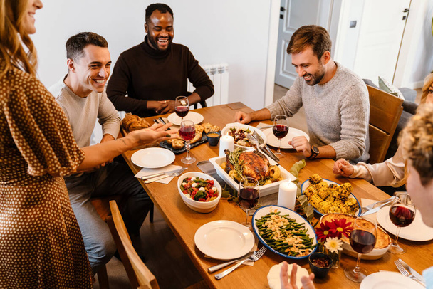 Multiracial happy friends eating turkey during thanksgiving dinner at home - Photo, Image