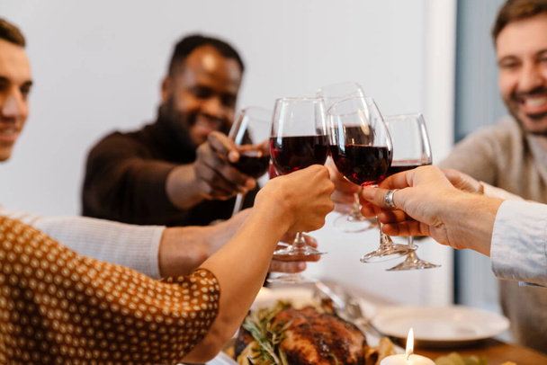 感謝祭の夕食の間にワインを飲む多人種の幸せな友人家で - 写真・画像