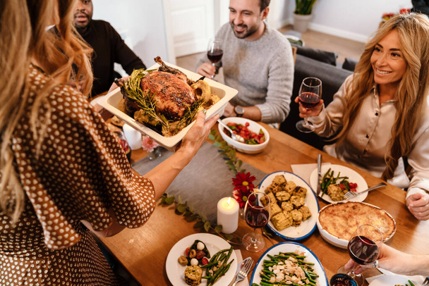 Multiracial happy friends eating turkey during thanksgiving dinner at home - Photo, Image