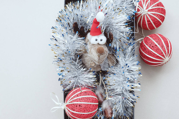 Un drôle de petit cerf jouet aux yeux bombés se trouve dans une moule argentée avec des boules de Noël rouges. Décor de Noël. - Photo, image