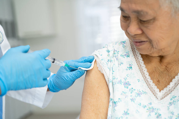 Ältere asiatische Seniorin mit Gesichtsmaske bekommt Covid-19 oder Coronavirus-Impfung vom Arzt gespritzt. - Foto, Bild