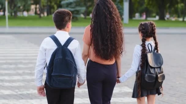 Powrót widok odpowiedzialny matka kobieta trzyma ręce dzieci syn i córka prowadzi uczniów z plecakami do szkoły stanąć na przejściu dla pieszych przejście na drodze rozejrzeć się przestrzegać przepisów ruchu drogowego - Materiał filmowy, wideo