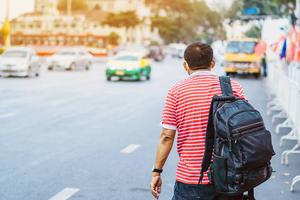 Visszapillantás a férfi beteg maszk piros-fehér ing egy fekete hátizsák áll a buszmegálló és integetett a kezét Taxi vagy busz a városban, hogy menjen a kórházba. - Fotó, kép