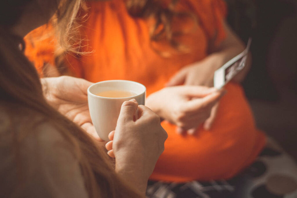 беременная молодая женщина, сидящая на кухне с подругой показывает фото открытки ультразвука снимок, дружественной концепции общения - Фото, изображение
