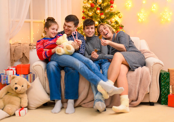 Winter holiday concept - Family sitting on a couch and posing in new year or christmas decoration. Children and parents. Holiday lights and gifts, Christmas tree decorated with toys. - Photo, image