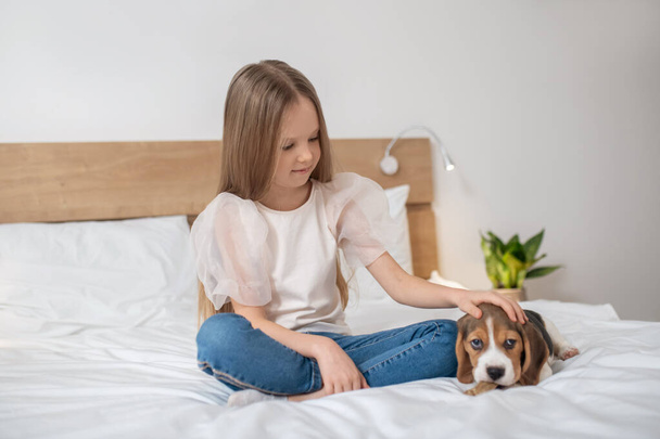 Sweet girl sitting on bed and playing with her puppy - Photo, image