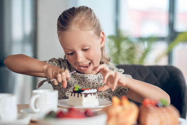 A cute blonde girl looking anticipated while looking at the slice of cake - Фото, изображение