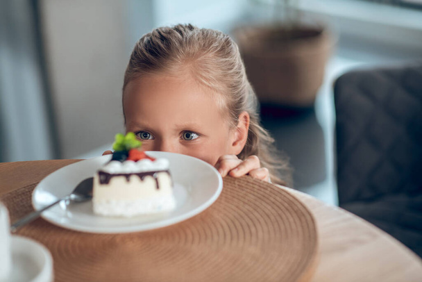 A cute blonde girl looking anticipated while looking at the slice of cake - Zdjęcie, obraz