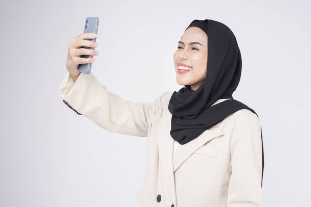 Portrait of young beautiful muslim woman in suit using smart phone over white background	 - Valokuva, kuva