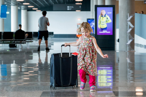 Cute blonde girl with travel luggage at the airport. - 写真・画像