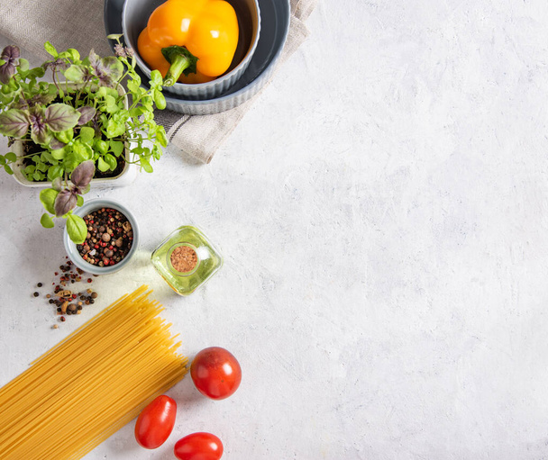 Consept plat lag met rauwe spaghetti met tomaten, basilicum, peper en olijfolie op een witte bakstenen ondergrond. Traditionele ingrediënten voor het maken van Italiaanse pasta. Bovenaanzicht en kopieerruimte. - Foto, afbeelding