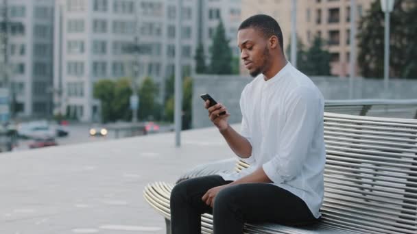 Zenci adam Bekleme randevusu sinirli Afro-Amerikan erkek afro-amerikalı erkek dışarıda oturur rahatsız hisseder. Etrafa bakar, birilerini ya da taksiyi gözetler ve geç saatlerde cep telefonuna bakar. - Video, Çekim