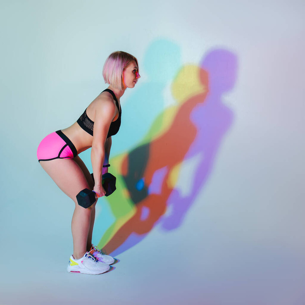 Stylish sports neon background. Sport modern woman exercising strong with dumbbells. fitness mood. Workout gym. Girl powerful in sportswear full height. Bodybuilding. Pink hair. fitness motivation - Photo, image