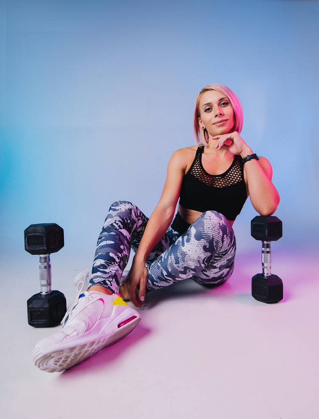 Stylish sports background. Sporty modern woman exercising with dumbbells strong with muscles. Blue fitness neon banner. Workout gym. Girl powerful in sportswear. Bodybuilding. Pink hair  - Photo, image