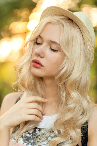 Close up profile portrait of a beautiful blonde woman with curly blonde hair and straw hat. - Foto, imagen