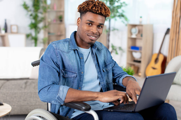 disabled young man sitting in wheelchair using laptop - Foto, imagen