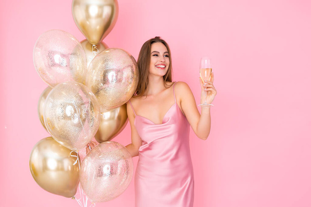 Smiling happy young woman raises up glass of champagne holds golden air balloons. Celebration - 写真・画像