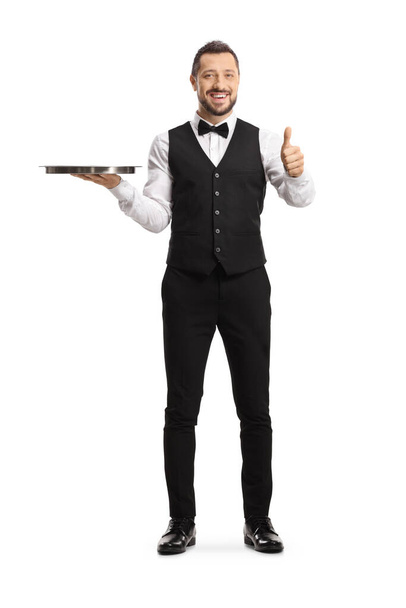 Full length portrait of a waiter holding a silver tray and showing thumbs up isolated on white background - Photo, Image