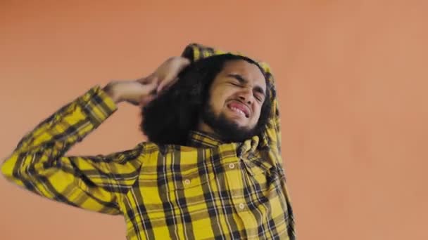 Een jonge man met een Afrikaans kapsel op een oranje achtergrond is moe. Emoties op een gekleurde achtergrond. - Video