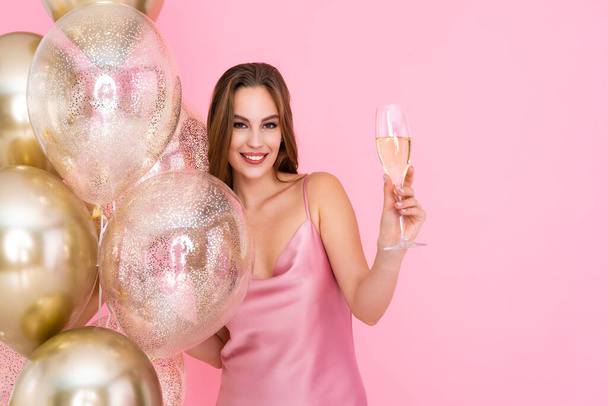 Half length of happy girl raises up glass of champagne stands near golden air balloons. Celebration  - Fotoğraf, Görsel