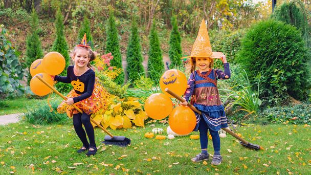 Malé čarodějky se učí létat s košťaty na venkovním Halloweenském večírku. Šťastné děti v karnevalových kostýmech s balónky bavit a hrát čarodějnice v podzimní sezóně. Děti si hrají na čarodějnice na koštěti. - Fotografie, Obrázek