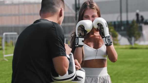 Молода жінка, яка тренуються до боксу зі своїм тренером, стукає в мітли з коліном
 - Кадри, відео