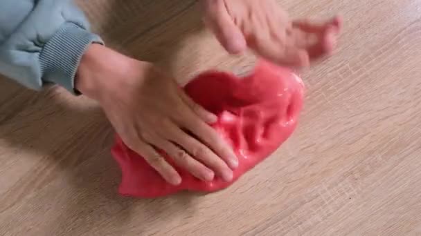 Playing with slime, stretching the gooey substance for fun and stress relief. Close up and top view of female hand holding red shining slime and squeezing it. Full HD slow motion video - Footage, Video
